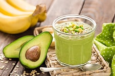 Avocado and banana smoothie with oats with ingredients in glass jar on wooden background.