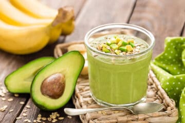 Avocado and banana smoothie with oats with ingredients in glass jar on wooden background.