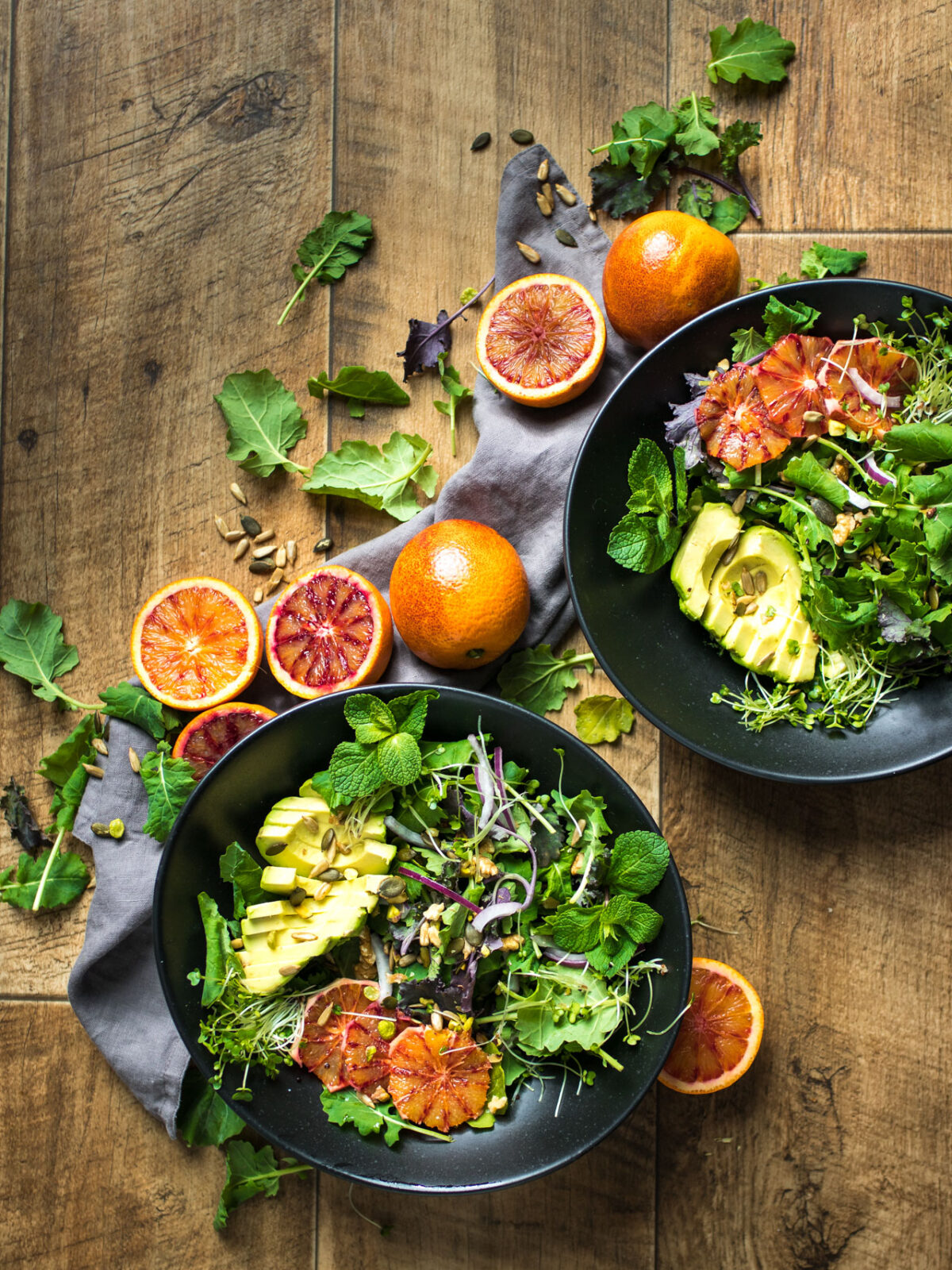 A delicious, winter salad featuring blood oranges and balsamic vinegar on black plates on a wooden table with blood oranges cut in half.