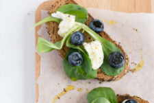 cropped image of two slices of bread adorned with fresh blueberries, caprese leaves, and mozzarella, drizzled with olive oil