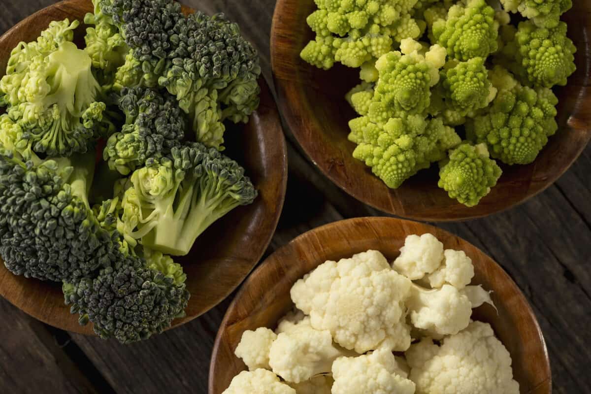 Fresh pieces of romanesco broccoli, broccoli and cauliflower in small rustic wooden bowls.