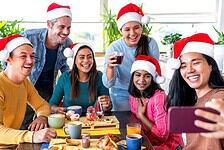 A group of people wearing Santa hats are sitting and standing around a table with breakfast food.