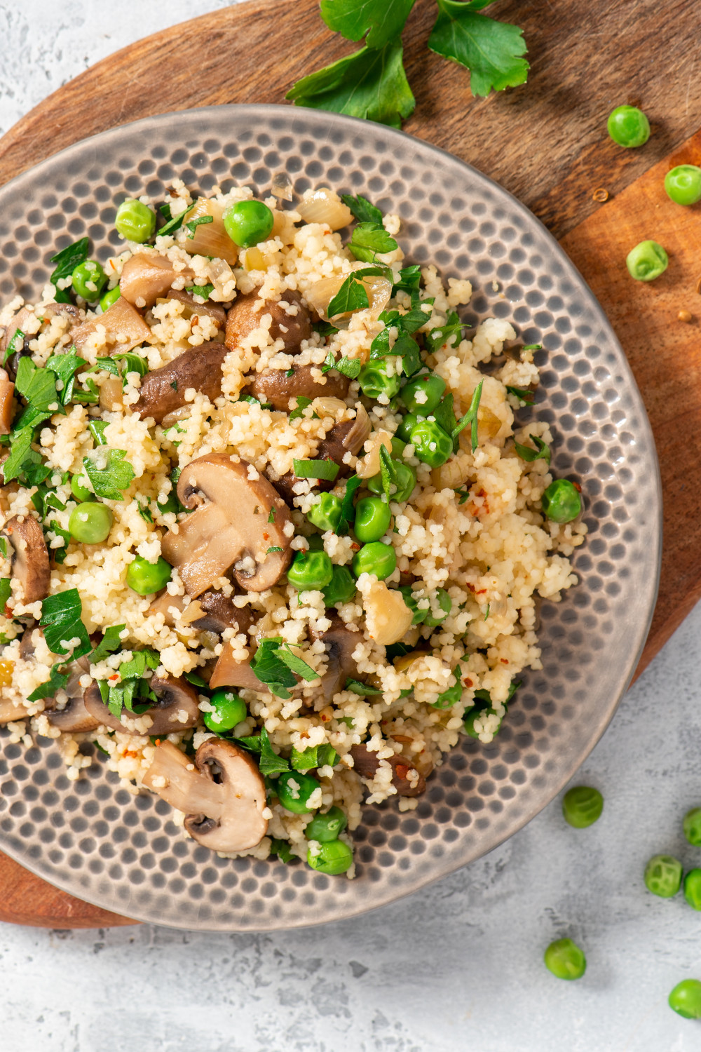 Couscous with fried mushrooms, onions, green peas, and parsley in a plate on a grey background top view.