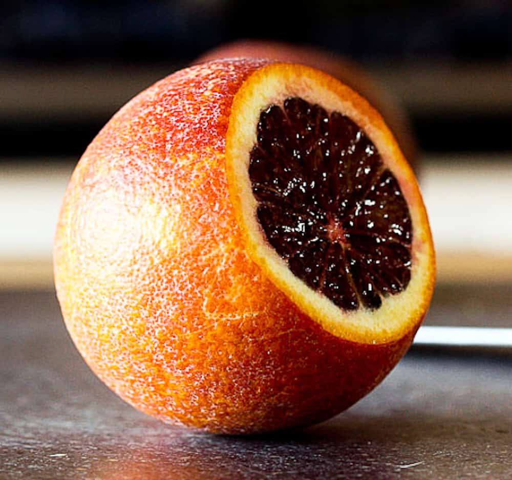 A Moro blood orange with a slice cut out on a countertop.