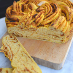 cropped image of a freshly baked sweet potato and sun-dried tomato braided bread resting on a cutting board, with two slices cut from it
