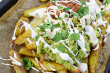 cropped image of a potato wedges nachos topped with guacamole, salsa and sour cream