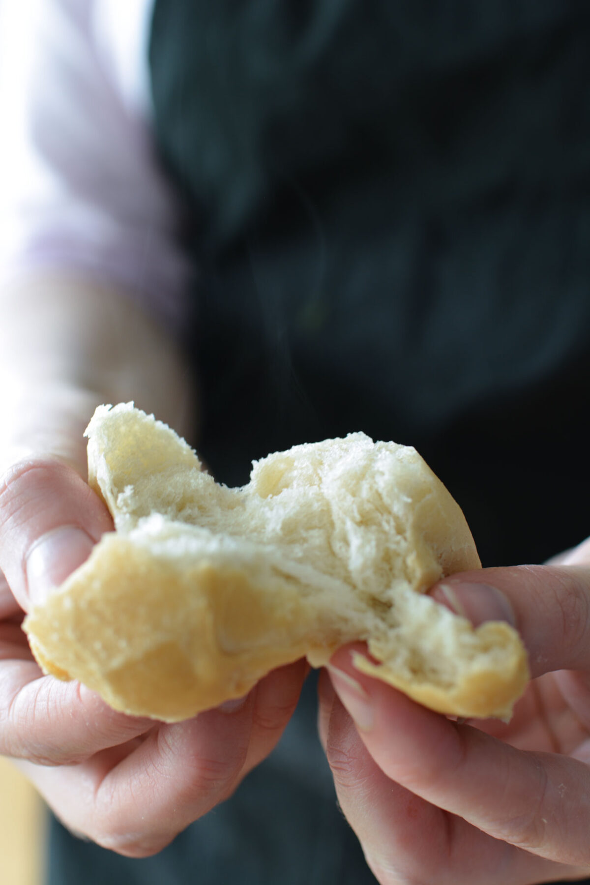 A close-up image of a woman's hands breaking open a freshly baked doughball, revealing the textured interior.