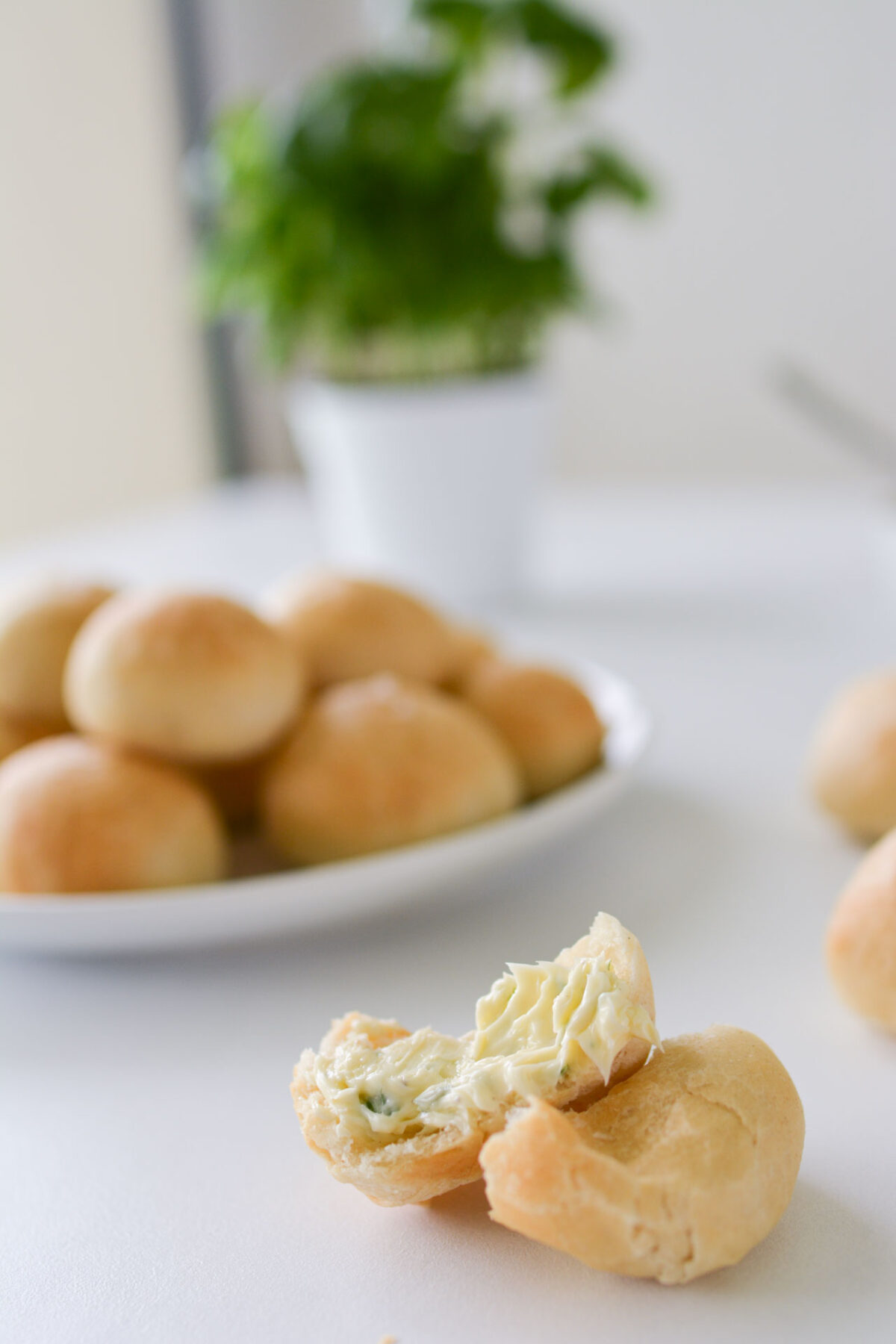 A close-up image of a single doughball featuring a flavorful homemade garlic butter, with a plate full of neatly arranged doughballs in the background.
