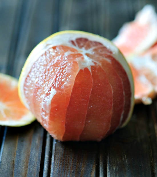 A pink grapefruit half peeled on a wooden table. 