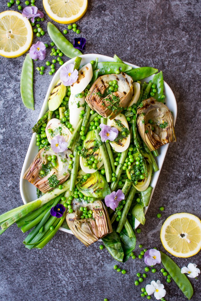 top down photo of a serving dish containing grilled spring vegetables including french green beans, spring onions, sugar snap peas, asparagus, leeks, and artichokes, glisten with a homemade lemon parsley butter