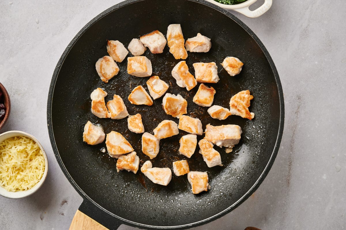 Chunks of chicken breast being browned in a skillet with some olive oil.