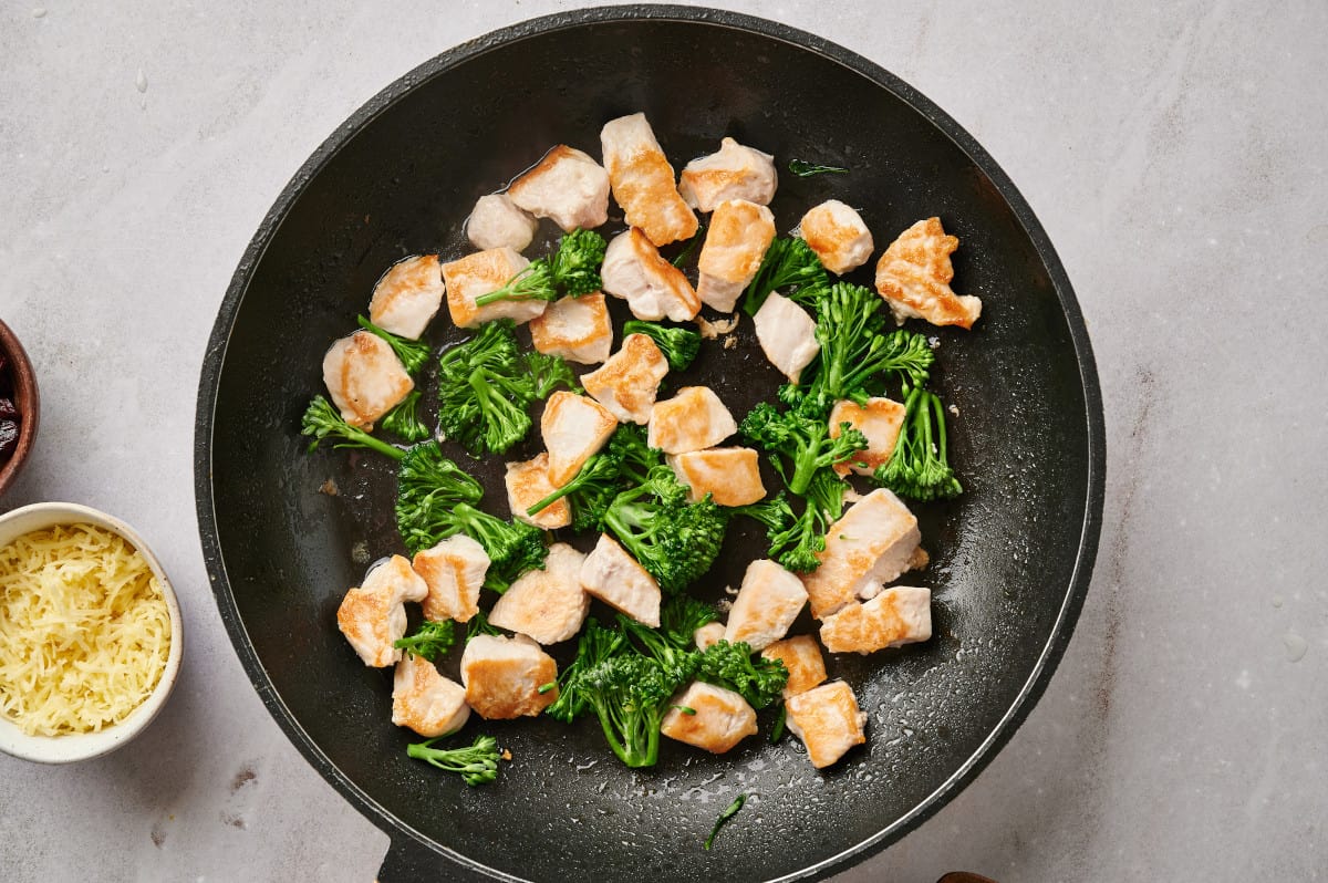 Chunks of chicken breast and broccoli being sautéed in a skillet.