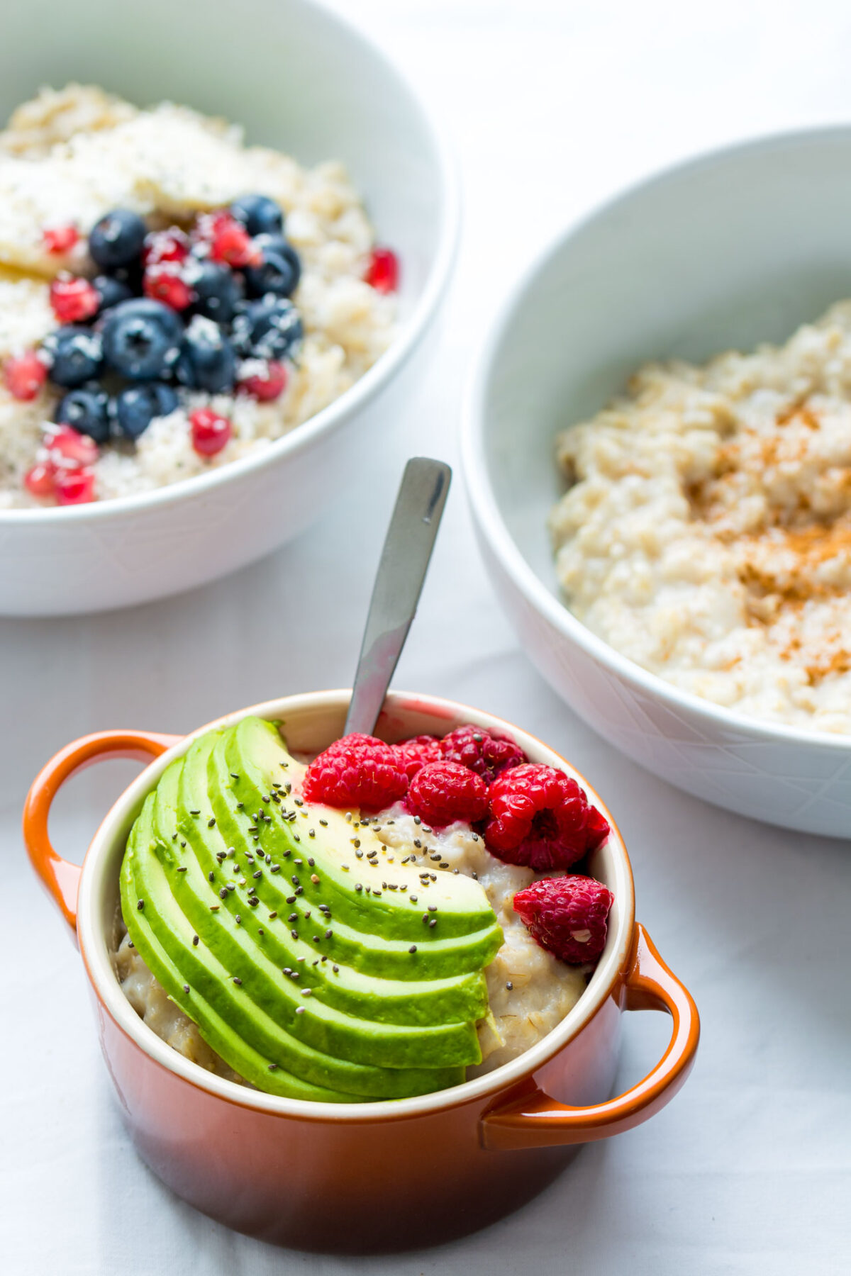 an image of a bowl containing an oatmeal topped with fresh slices of avocado and raspberries