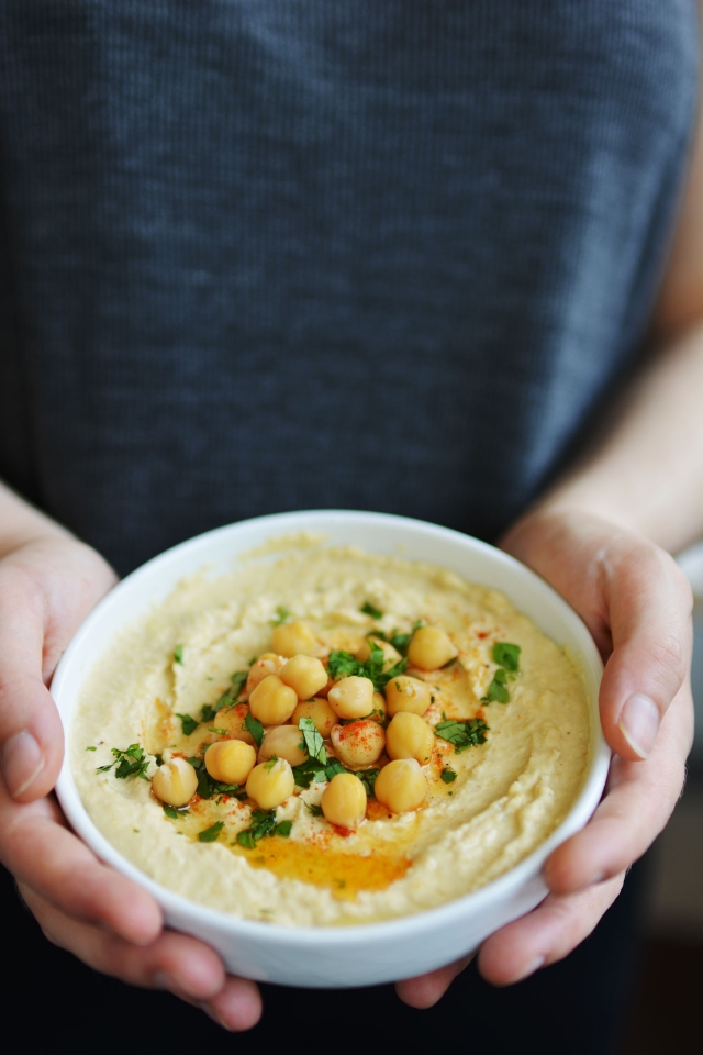 hands holding a bowl of freshly cooked hummus 