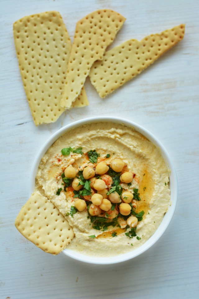 hummus recipe in a bowl topped with checakpeas and a piece of cracker 
