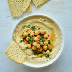 hummus recipe in a bowl topped with checakpeas and a piece of cracker