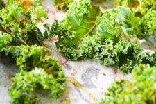 a baking tray filled with fresh kale leaves, evenly coated with seasonings