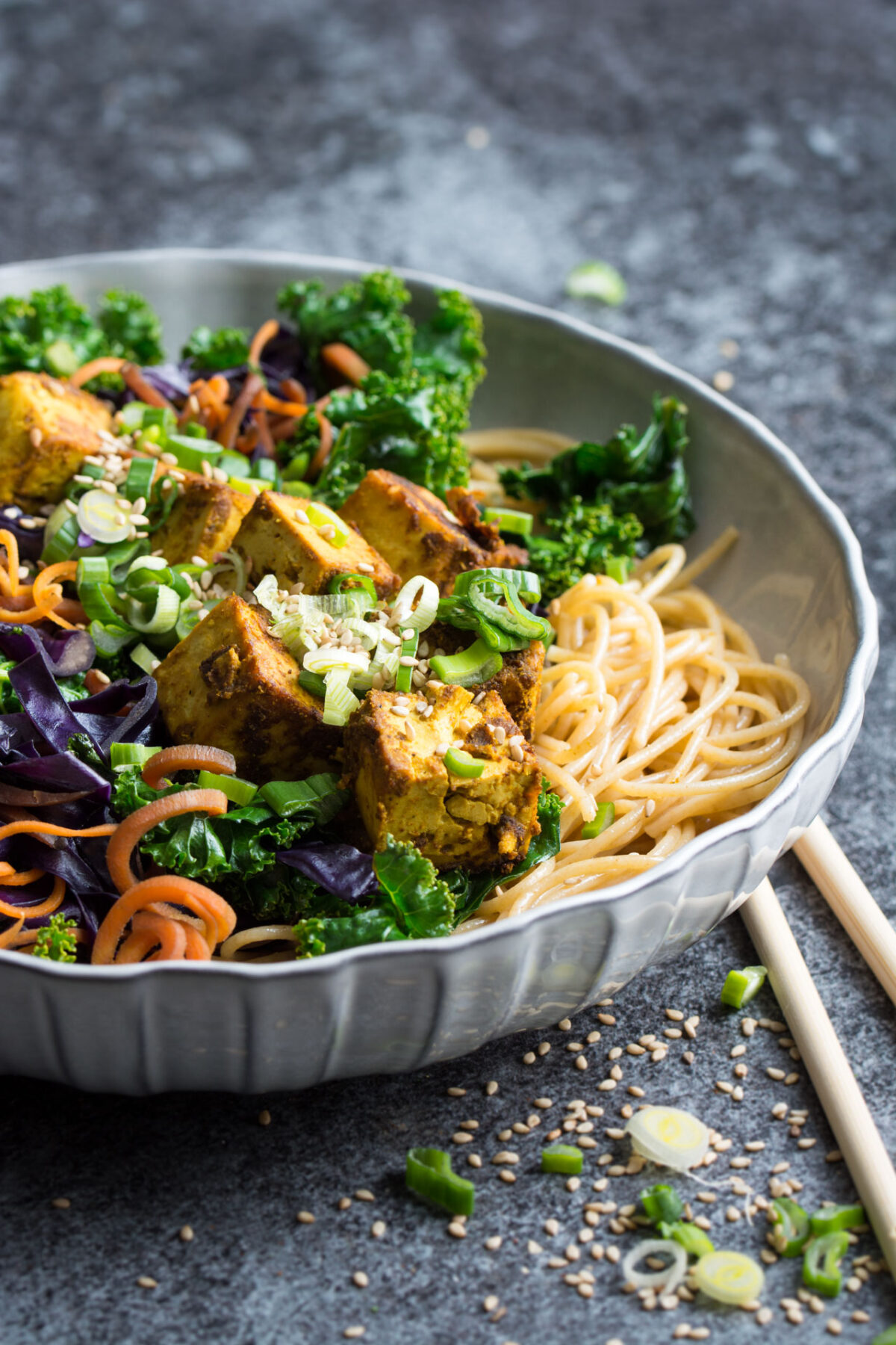 A bowl is filled with a nutritious kale stir fry with crispy curried tofu with chopsticks laying on the side.
