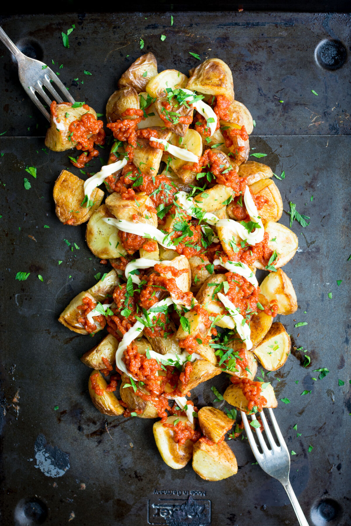 Patatas Bravas on a griddle sitting on a light colored background with two forks on the sides of the dish.
