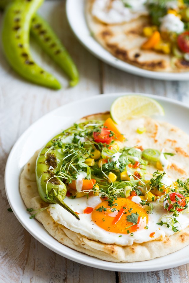 close up view of a naan bread in a plate top with sunny side up egg, sweet corn, cherry tomato, cress and grilled pepper