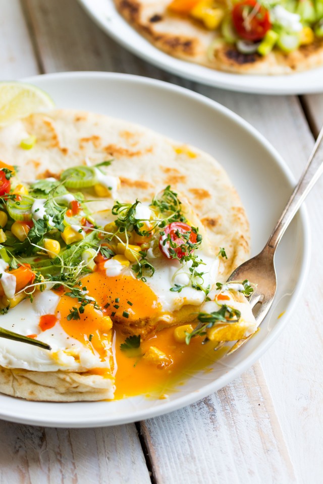 side view image of a fork presses a loaded naan bread, the egg yolk oozes and flows, adding a creamy and luscious texture to the dish.