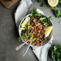 A white bowl filled with a Mediterranean quinoa salad with lemon wedges.
