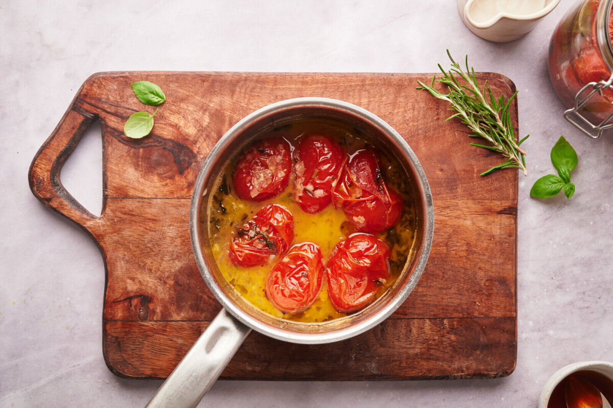 Roasted tomatoes and vegetable broth in a pot on a wooden cutting board.
