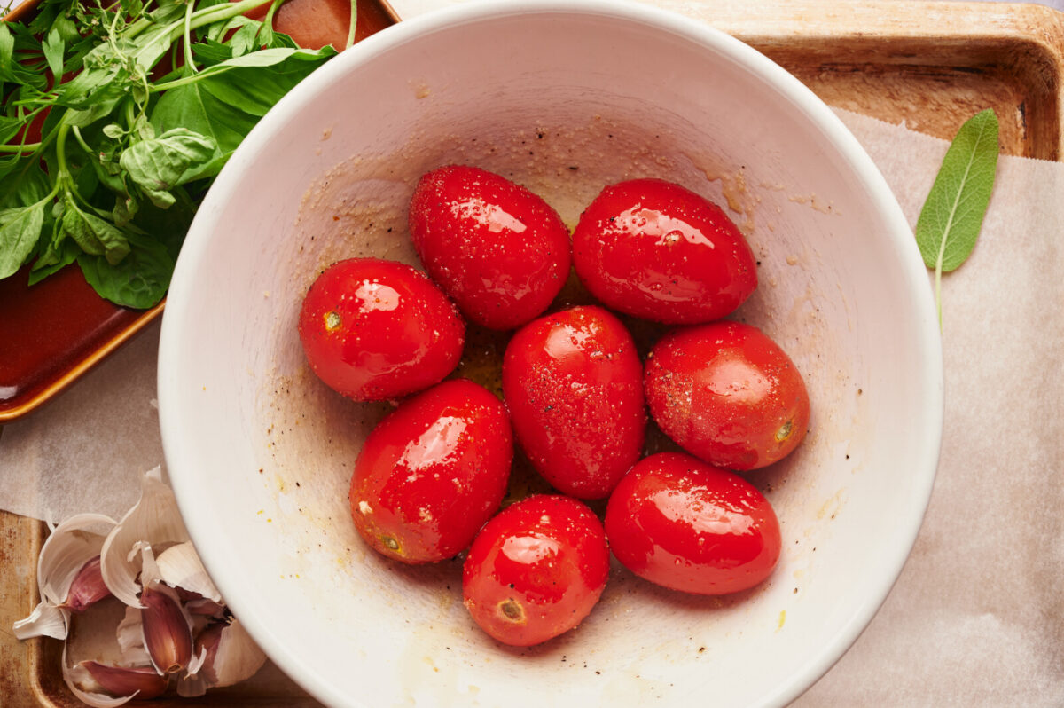 A white bowl filled with plum tomatoes that have been seasoned with garlic, olive oil, salt, and pepper.