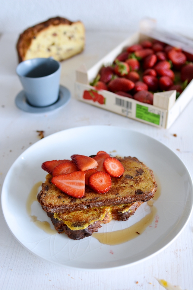 a plate featuring freshly toasted panettone slices, adorned with sliced strawberries and a generous drizzle of maple syrup