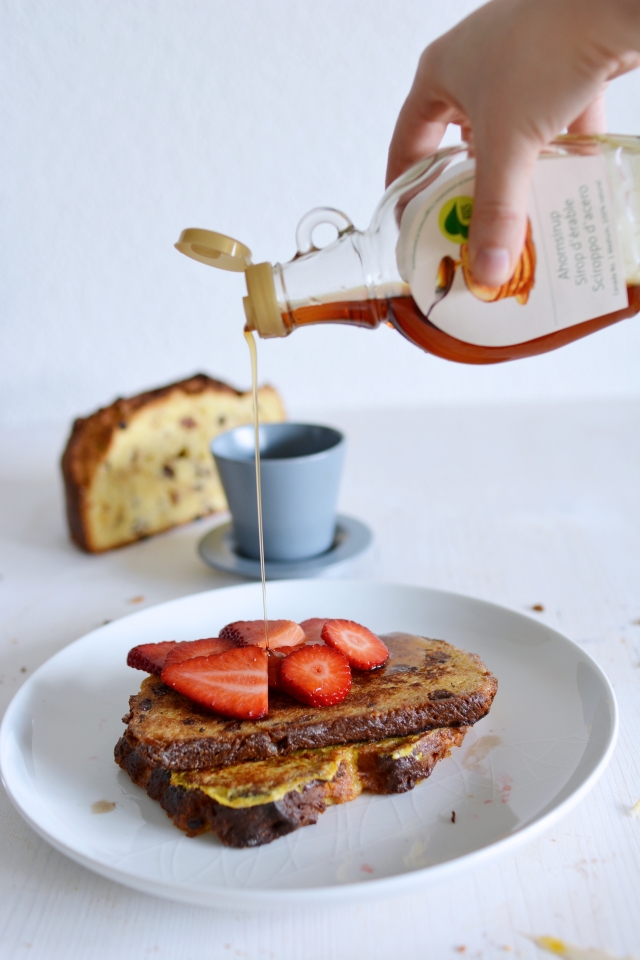 image of a hand drizzling maple syrup onto a plate of panettone french toast, garnished with fresh strawberry slices