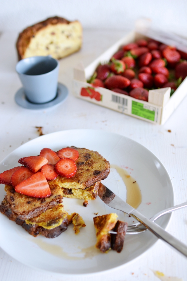 plate with panettone french toast, adorned with sliced fresh strawberries, being cut with a knife and fork