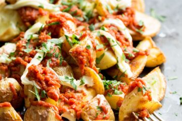 Patatas Bravas covered in tomato sauce and drizzled with mayonnaise and green herbs close up.