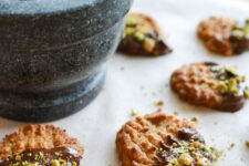 cropped image of Flourless Peanut Butter, Chocolate and Pistachio Cookies flourless peanut butter, chocolate, and pistachio cookies arranged flat on parchment paper, with a stone and mortar and pestle beside them