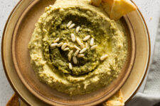 close up image of a pesto hummus in a round plate with pita chips