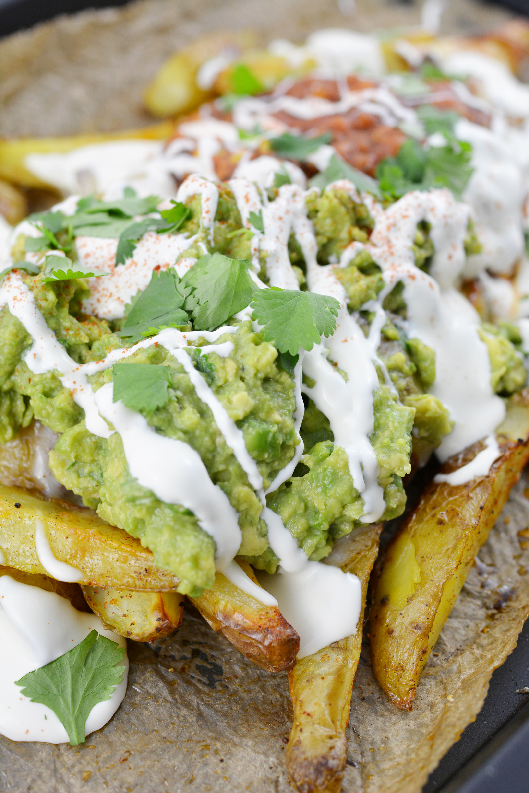 close-up image of potato wedge nachos featuring a generous serving of guacamole and a drizzle of sour cream on top 