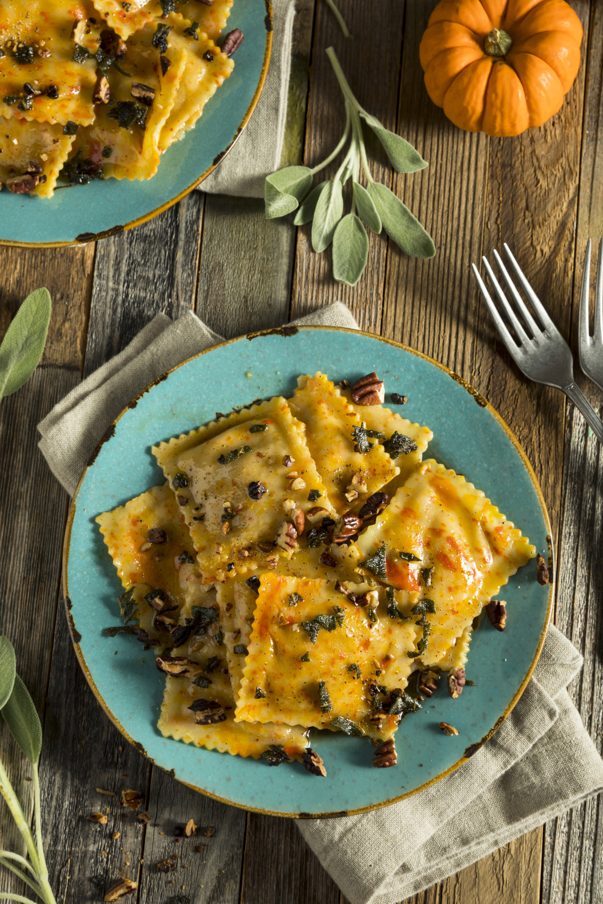 Vertical view of pumpkin ravioli with a small pumpkin and sage on a wooden table.