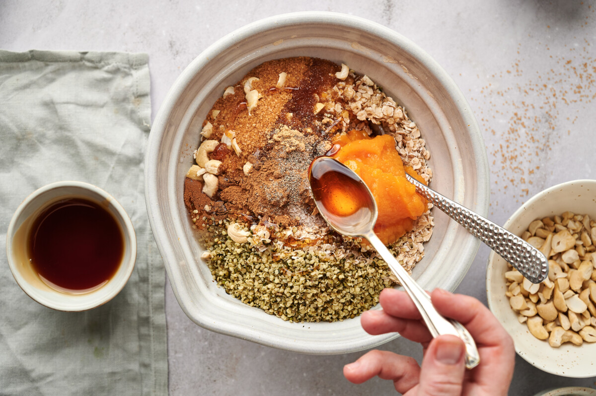 Mixing up ingredients for Pumpkin Spice Granola and adding some maple syrup with a spoon.