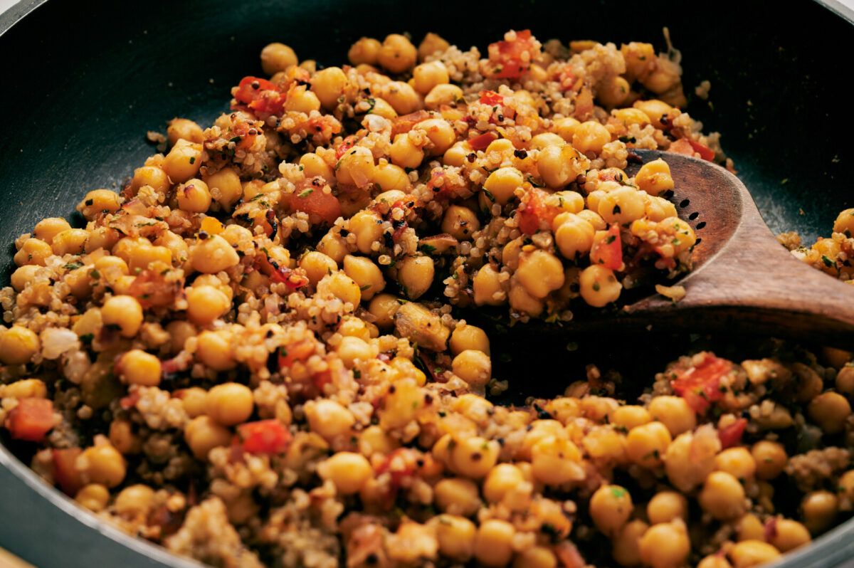 Quinoa and chickpea stuffing mixture in a black skillet with a wooden spoon.