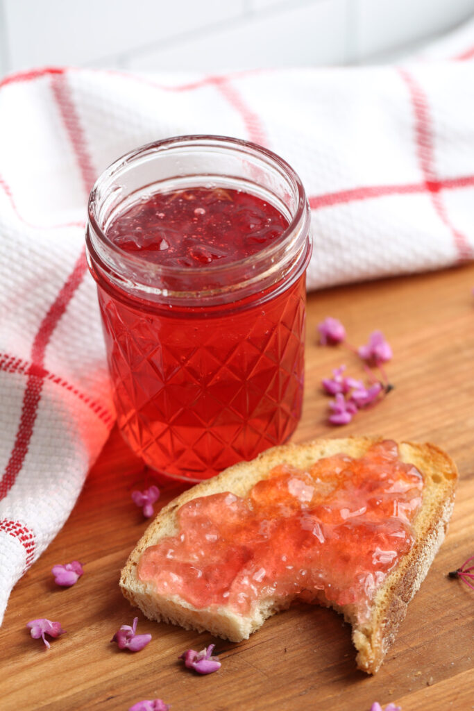 Redbud jelly in a jar with a piece of toast with a bite taken.