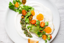 top down image of savory yogurt chimmichurri salad, topped with spicy roasted chickpeas, slice avocado, tomatoes and eggs on the side