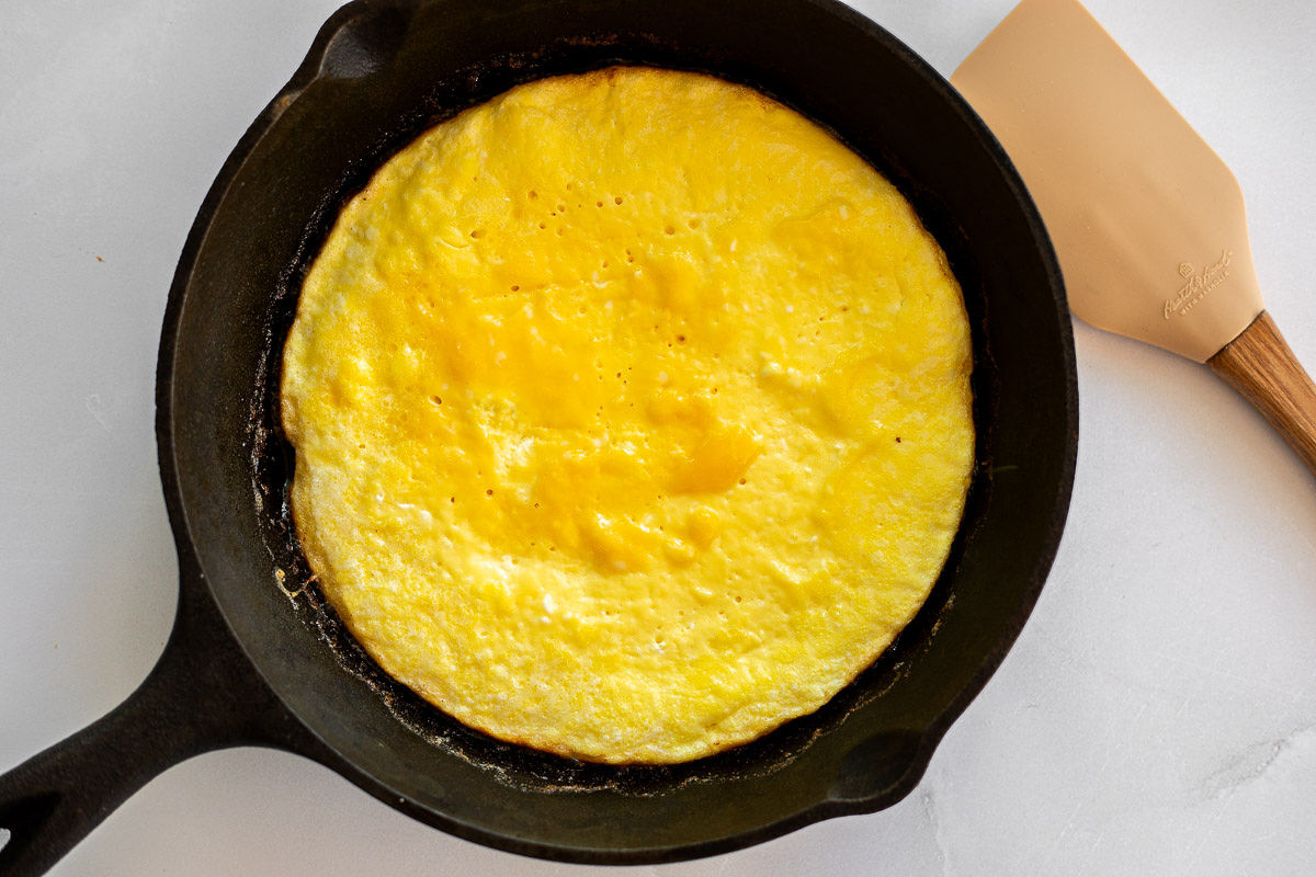 An omelet cooking in a skillet with a spatula. 