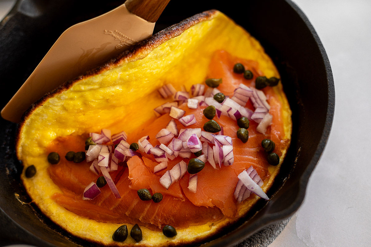 A skillet with an omelet filled with smoked salmon, red onions, and capers.