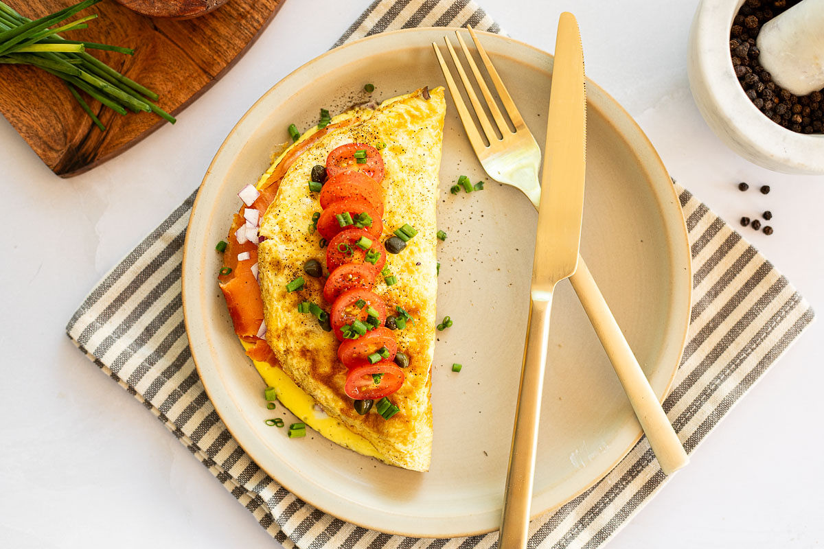 A plate with an omelet filled with smoked salmon and topped with a sliced tomato. 