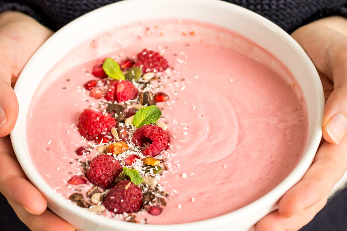 A pink berry smoothie bowl being held in a woman's hands.