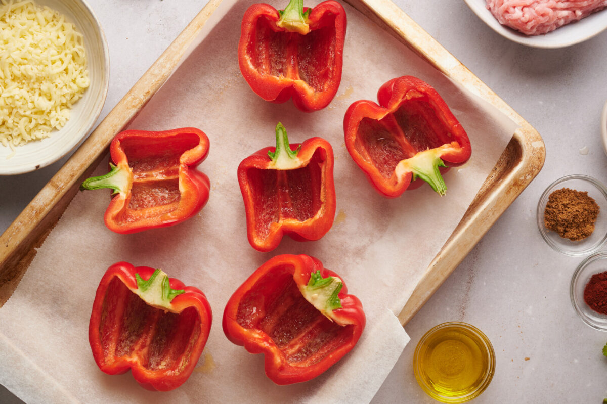 Red bell peppers sliced in half vertically and placed on a parchment lined baking sheet, cut side up.