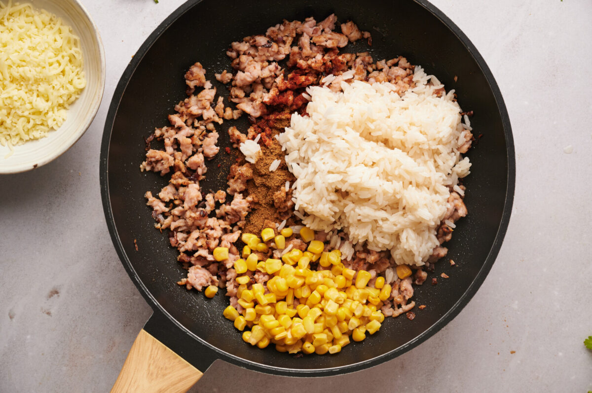 White rice corn and spices added to ground turkey in a skillet.