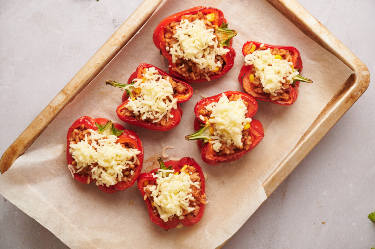 Stuffed red bell peppers with mozzarella cheese on top arranged on a parchment lined baking sheet.