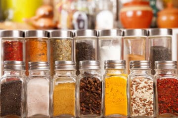 Glass containers of a variety of spices arranged in orderly rows.