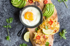 cropped image of spicy sweetcorn and potato fritters lay flat in the chopping board with sliced avocado and sunny side up egg