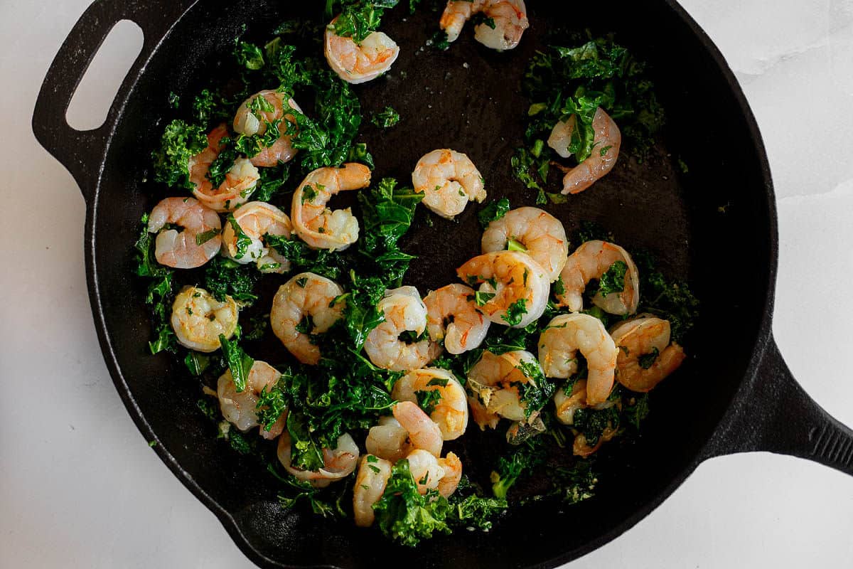 Shrimp and kale being sautéed in a cast iron skillet.